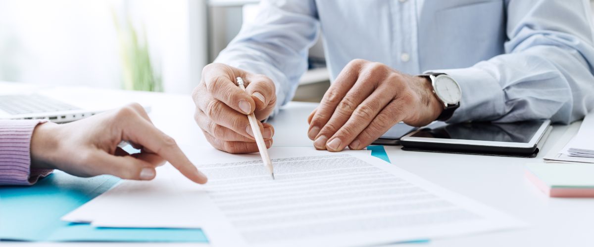 A woman and a man are going through a contract. Only their hands are visible; the man is holding a pencil (illustrative image).